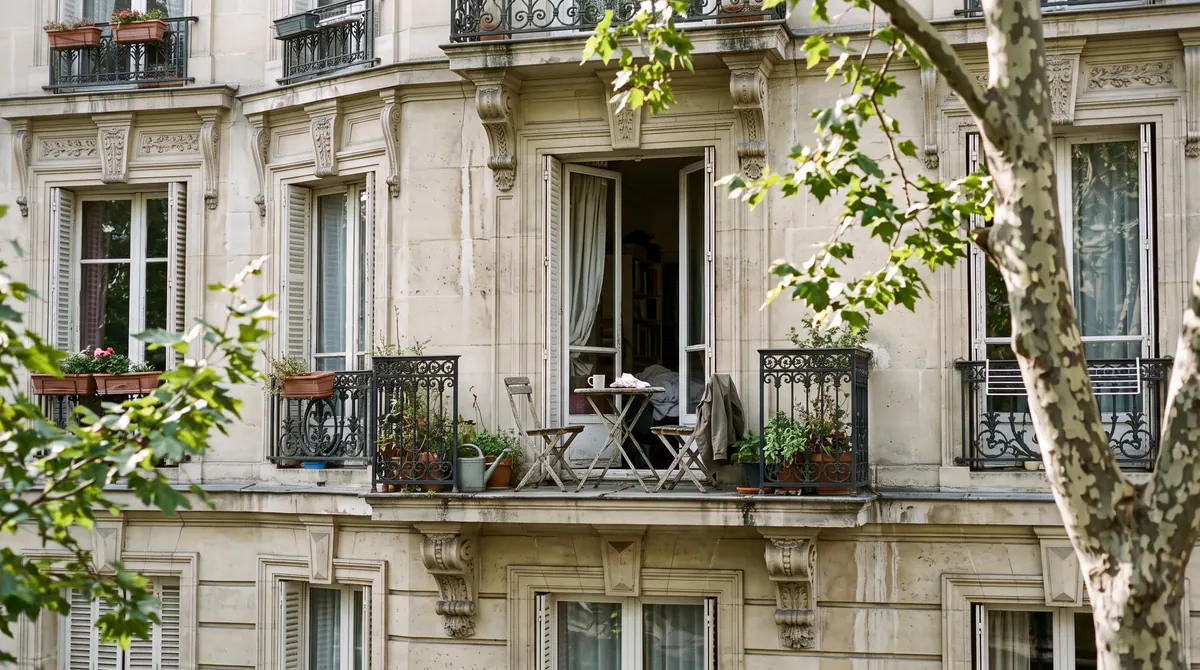 Immeuble haussmannien à Paris, balcon en fer forgé avec une petite table et deux chaises, platane et une fenêtre ouverte le matin